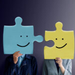 Due persone tengono in mano due pezzi di puzzle che si incastrano, con sopra disegnate due faccine sorridenti