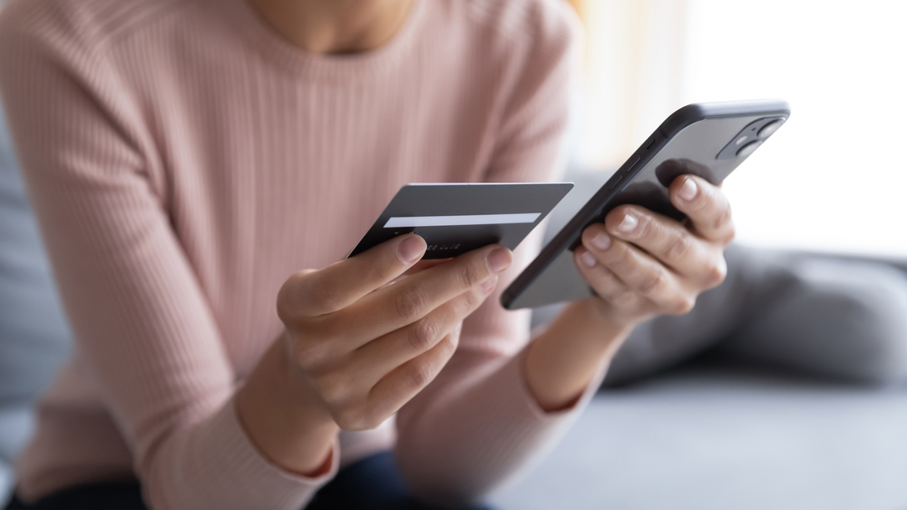 CLOSE UP SULLE MANI DI UNA DONNA CHE UTILIZZA UNO SMARTPHONE ED UNA CARTA DI CREDITO